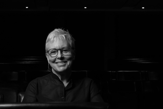 Black and white portrait of a person wearing glasses and dark clothing against a dark background.