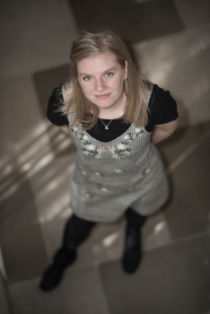 Woman looking down at camera from above, wearing gray sweater and black long-sleeve shirt.