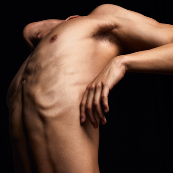 Shirtless male torso with defined musculature against dark background, arms positioned across body.
