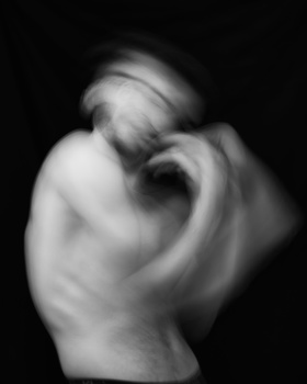 Monochromatic studio portrait of a curled human figure with dramatic chiaroscuro lighting.