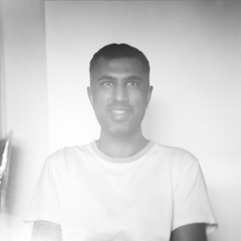Black and white portrait of a man wearing a light-colored t-shirt against a plain wall.