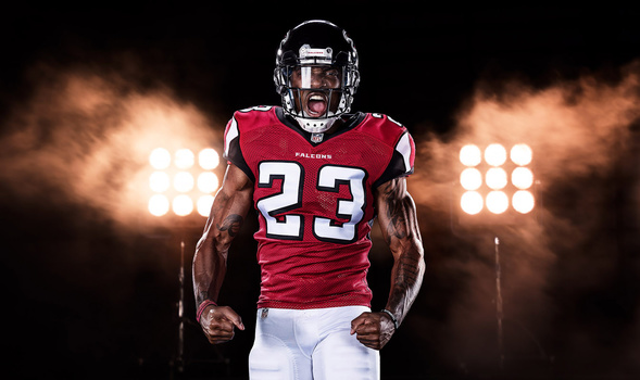 Football player wearing red Falcons jersey number 23 in dramatic stadium lighting with smoke effects.
