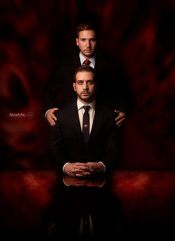 Two men in formal black suits posed against a dramatic red and black textured background.