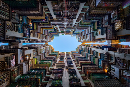 Upward view of dense high-rise residential buildings framing a bright blue sky in the center.