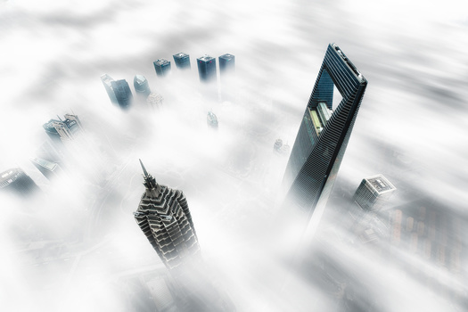 Tall skyscrapers rising above thick fog and clouds in an urban landscape.