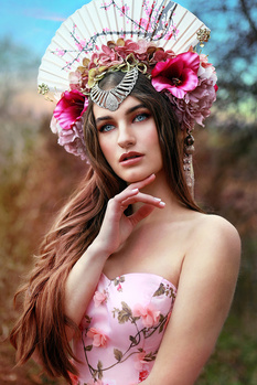 Woman wearing an ornate floral headdress and pink floral top against a blurred natural background.