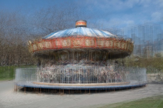 Abandoned carousel with peeling paint and metal fencing in an overgrown urban park.