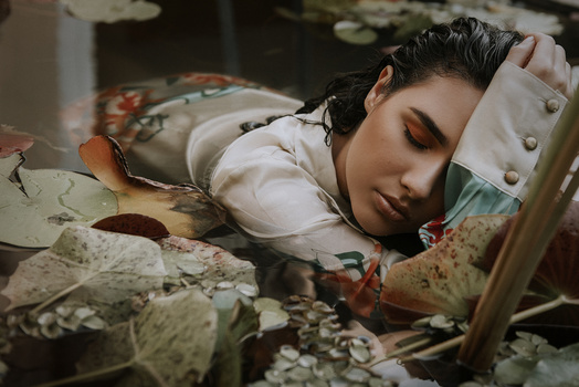 Person resting head on hand surrounded by scattered autumn leaves and foliage.