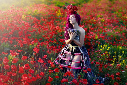 Woman in elaborate purple gown standing in vibrant red poppy field during golden hour.