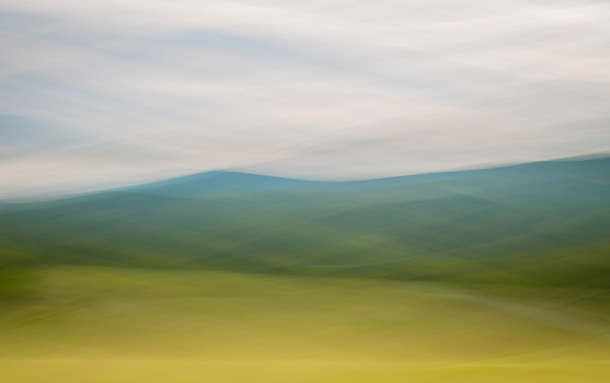 Soft-focus landscape with layered hills fading into a hazy horizon beneath overcast sky.