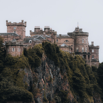 Medieval castle perched on a rocky cliff covered in green ivy and vegetation.