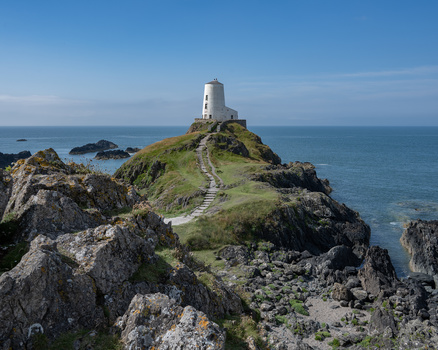 White lighthouse perched on a rocky coastal promontory surrounded by turquoise waters.