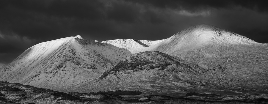 Snow-covered volcanic mountains with dramatic storm clouds overhead in high-contrast black and white photography.