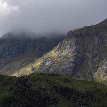 Misty mountainous landscape with steep rocky slopes and green vegetation under overcast sky.