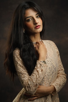 Woman with long dark hair wearing an embroidered cream cardigan against a dark background.