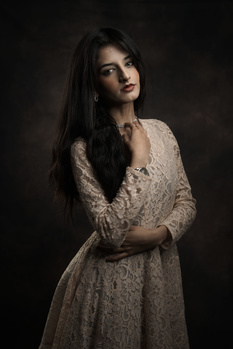 Woman with long dark hair wearing a beaded cream-colored dress against a dark background.