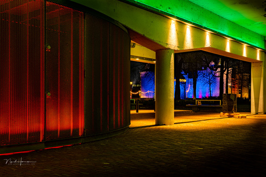 Modern architectural storefront with vibrant red mesh panels on left and illuminated blue-toned display windows on right.