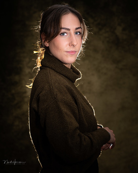 Woman in dark sweater looking over shoulder against muted golden-brown backdrop.