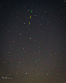 Bright meteor streaking across a starry night sky above a dark landscape.