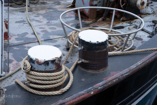 Two weathered bollards with coiled rope on a ship's deck covered in snow and ice.