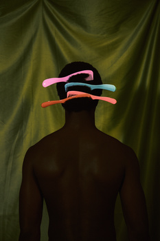 Silhouetted figure with colorful gels balanced horizontally across shoulders against draped green backdrop.