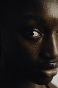 Close-up portrait of a person's face lit from the side against a dark background.
