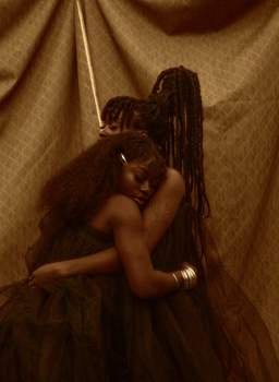 Two figures with long dark hair embracing against a draped gold fabric backdrop.