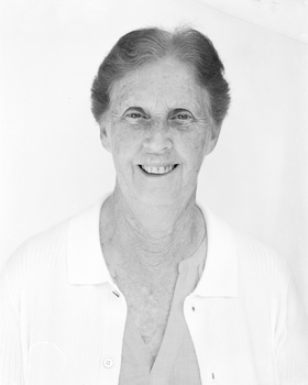 Black and white headshot portrait of a smiling man wearing an open white shirt.