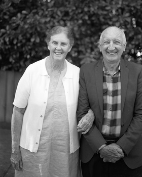 Two people smiling at camera in outdoor black and white portrait photograph.