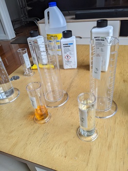 Laboratory glassware and chemical bottles arranged on a wooden table.
