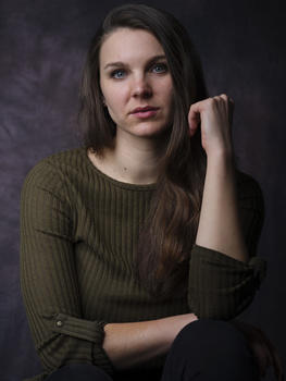 Woman with long dark hair wearing an olive ribbed sweater against a dark textured background.