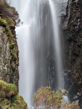 Waterfall cascading down between moss-covered rock cliffs with soft, misty water flow.