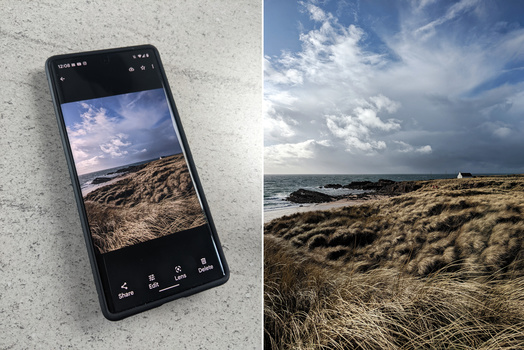 Smartphone displaying a coastal landscape photo next to the full-scale scene of grassy dunes and ocean.