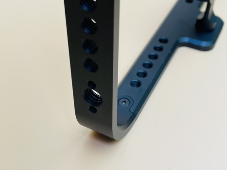 Two metal mounting brackets with multiple circular holes arranged vertically, one black and one blue, positioned at an angle on a white surface.