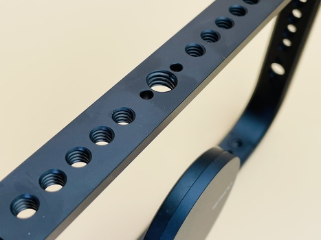 Close-up of a metal perforated plate with evenly spaced threaded holes and a curved metal strap.