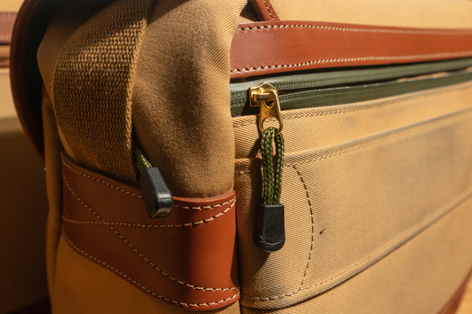 Close-up of leather camera bag strap and zipper with brass hardware and canvas fabric detail.