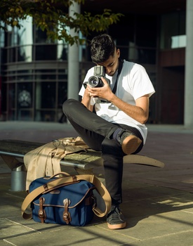 Photographer seated outdoors holding a film camera, with camera bags positioned on the ground.