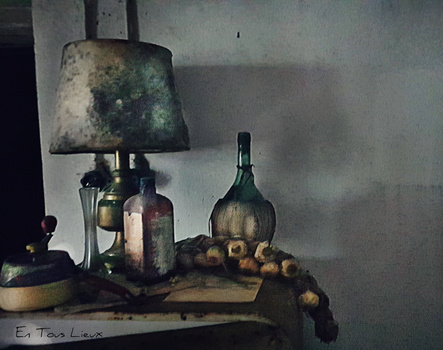Still life arrangement with table lamp, wine bottles, and woven basket under warm, directional lighting.