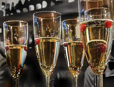 Four champagne flutes with varying fill levels against a dark background with bokeh lights.