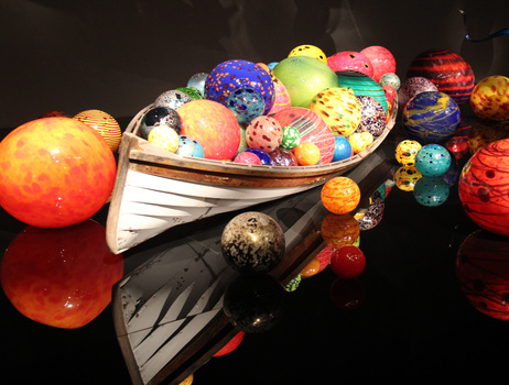 Colorful bowling balls arranged in and around a white rowboat on a reflective black surface.