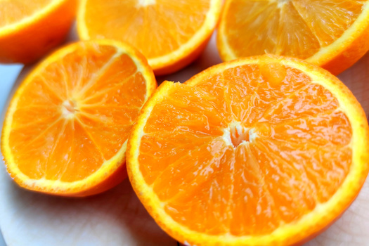 Fresh orange slices arranged on a white surface, showing bright citrus flesh and vibrant yellow-orange rind.