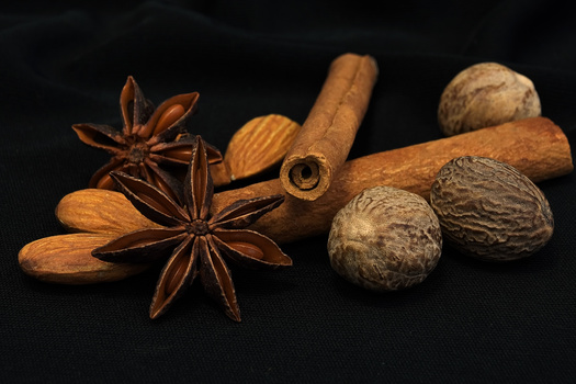 Star anise, cinnamon stick, almonds, and nutmeg arranged on black background.