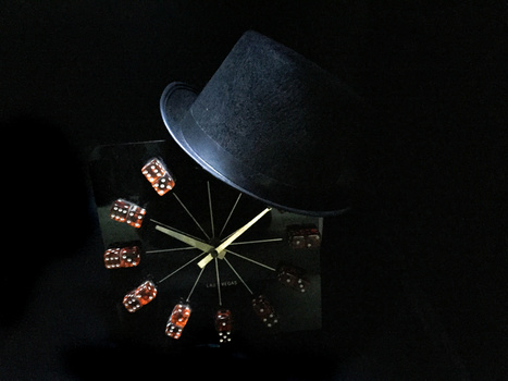 Overhead view of dice arranged in a circle around a centered fedora hat against a black background.