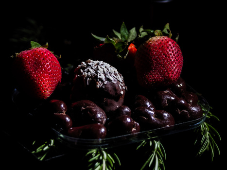 Ripe strawberries and dark cherries arranged on a black surface against a dark background.