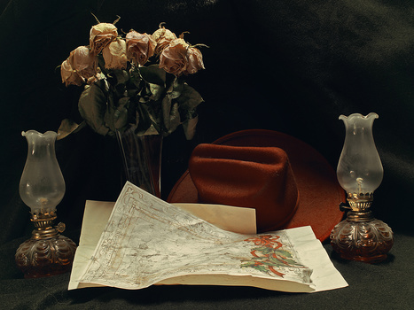 Still life arrangement with dried roses in vase, vintage lamps, and unfolded map on dark surface.