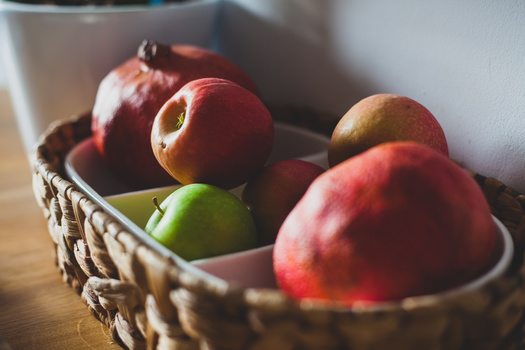 Red and green apples in a woven basket with warm, directional sunlight creating shadows and highlights.