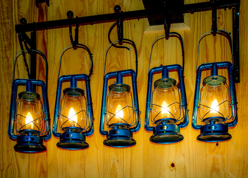Five blue vintage-style lanterns with glowing candles hung from a horizontal rod against a wooden wall.