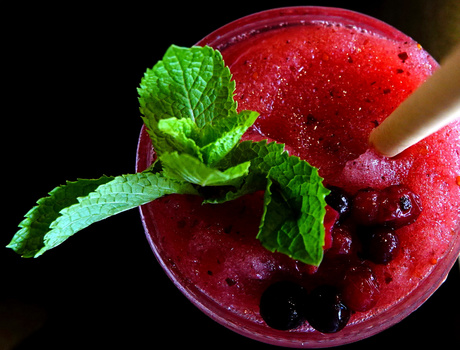 Red beverage garnished with fresh mint leaves, photographed against a dark background.