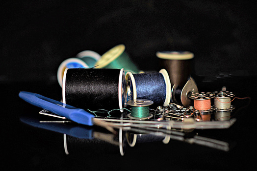 Sewing supplies arranged on a reflective black surface, including spools of thread, needles, scissors, and a thimble.