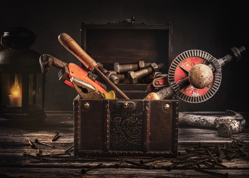 Vintage trunk filled with hunting rifle, ammunition, lantern, and tools arranged in dramatic overhead lighting.